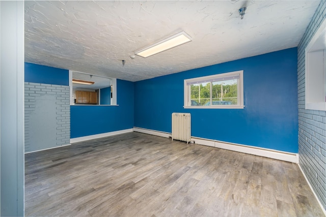 unfurnished room featuring hardwood / wood-style flooring, a textured ceiling, a baseboard radiator, and radiator heating unit