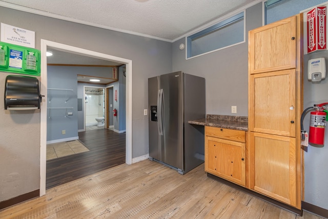 kitchen with dark stone counters, light hardwood / wood-style flooring, a textured ceiling, stainless steel refrigerator with ice dispenser, and ornamental molding