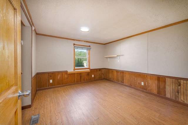 spare room with ornamental molding, wooden walls, light hardwood / wood-style floors, and a textured ceiling