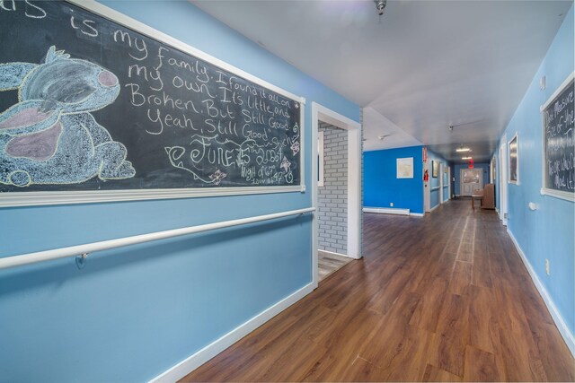 hall featuring wood-type flooring, baseboard heating, and brick wall