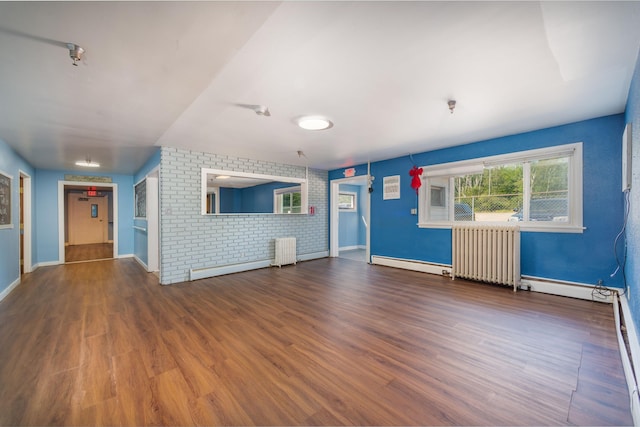 unfurnished living room featuring brick wall, radiator heating unit, a baseboard radiator, and wood-type flooring