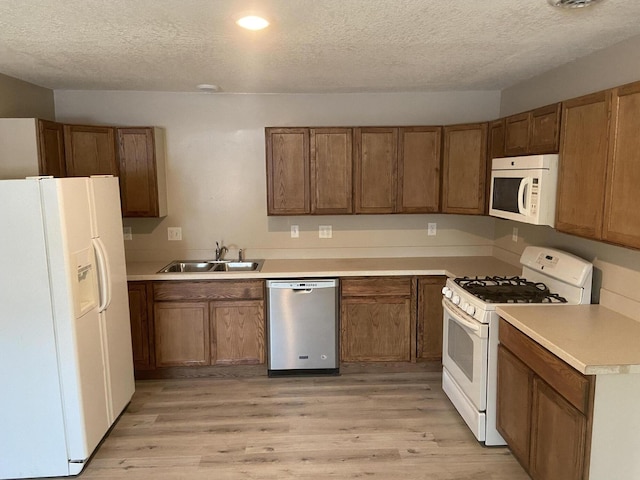 kitchen featuring sink, a textured ceiling, white appliances, and light hardwood / wood-style floors