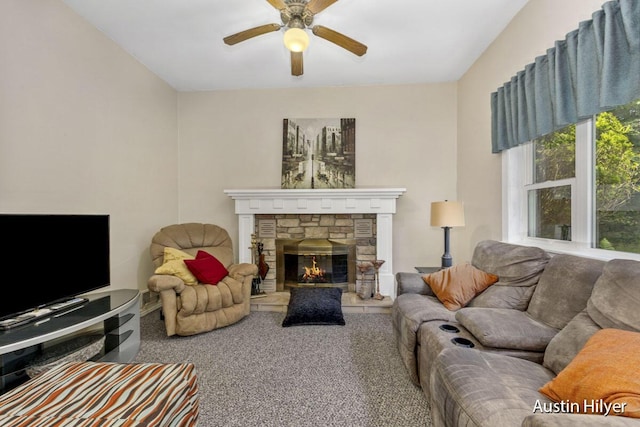 living room with a stone fireplace, carpet floors, and ceiling fan