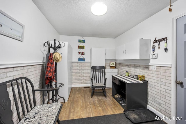 living area with brick wall, a textured ceiling, and light hardwood / wood-style floors