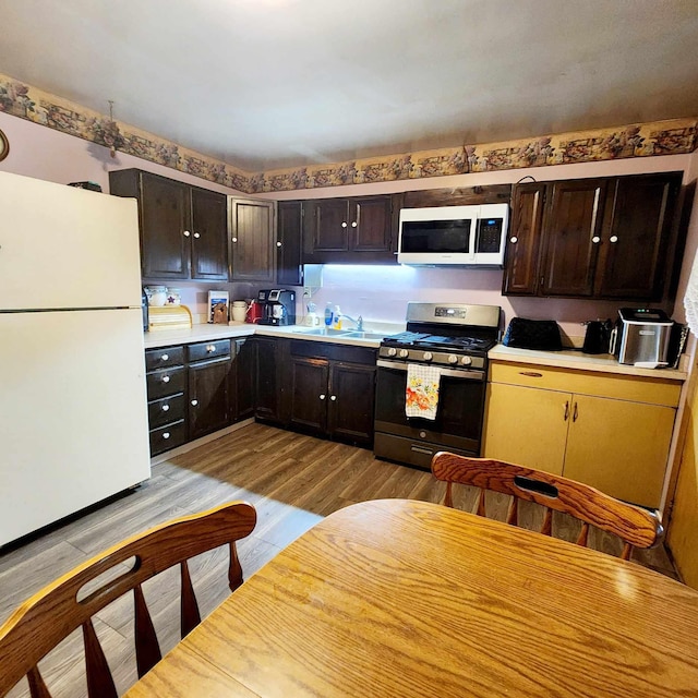 kitchen with white appliances, dark brown cabinetry, sink, and light hardwood / wood-style flooring