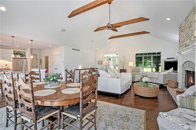 dining area featuring ceiling fan, beam ceiling, high vaulted ceiling, dark hardwood / wood-style floors, and a stone fireplace