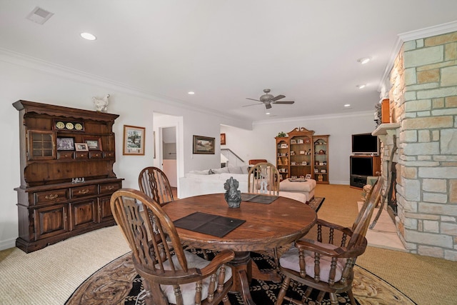 carpeted dining area featuring crown molding, ceiling fan, and a stone fireplace