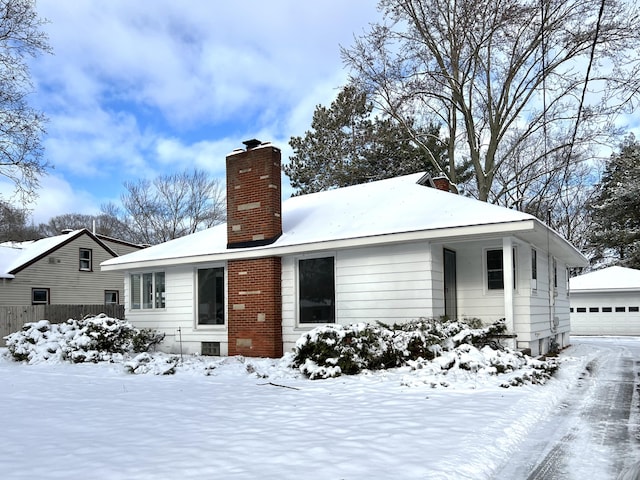 snow covered rear of property featuring a garage and an outbuilding