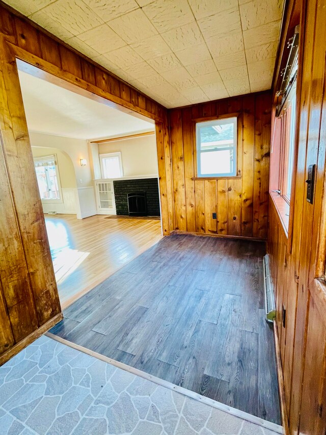 unfurnished living room with dark wood-type flooring, a wealth of natural light, a brick fireplace, and wood walls