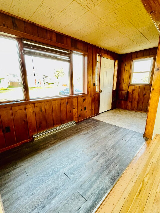 unfurnished room with a baseboard heating unit, wooden walls, and light hardwood / wood-style floors