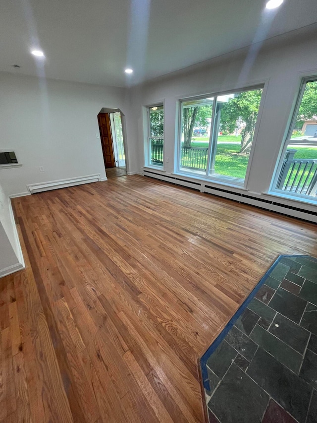 unfurnished living room with a baseboard heating unit and wood-type flooring