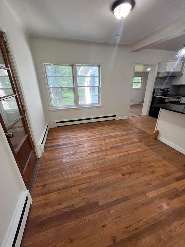 unfurnished living room featuring plenty of natural light, baseboard heating, and wood-type flooring