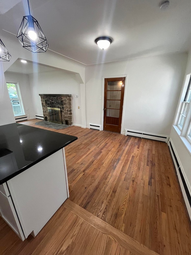 kitchen featuring decorative light fixtures, a baseboard heating unit, wood-type flooring, and a stone fireplace