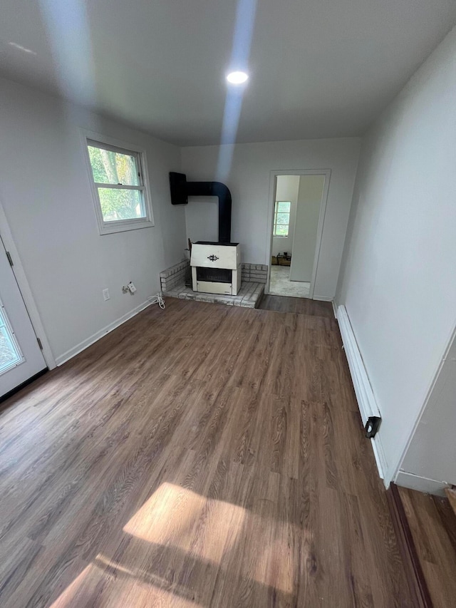 unfurnished living room with a wood stove, a baseboard heating unit, and hardwood / wood-style floors