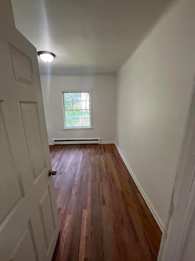 spare room featuring a baseboard heating unit and dark wood-type flooring