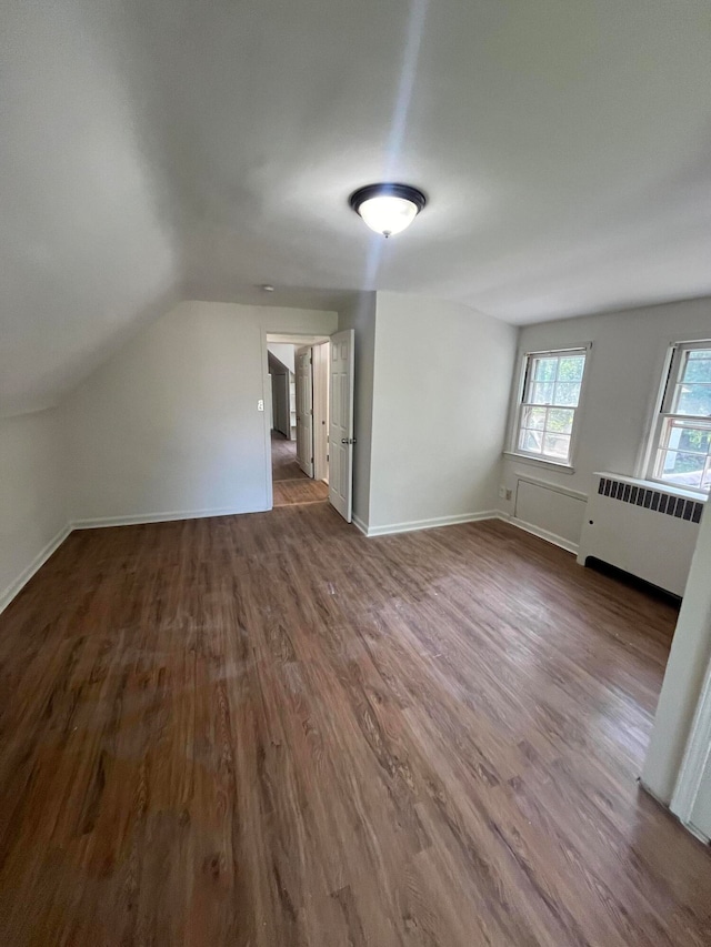 additional living space with radiator heating unit, wood-type flooring, and vaulted ceiling