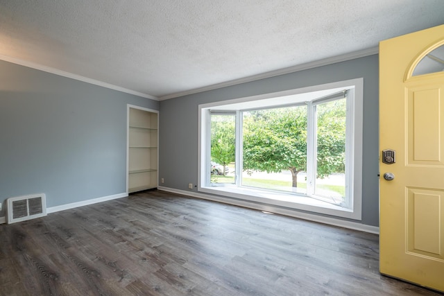 spare room featuring dark wood-type flooring, built in shelves, a wealth of natural light, and a textured ceiling