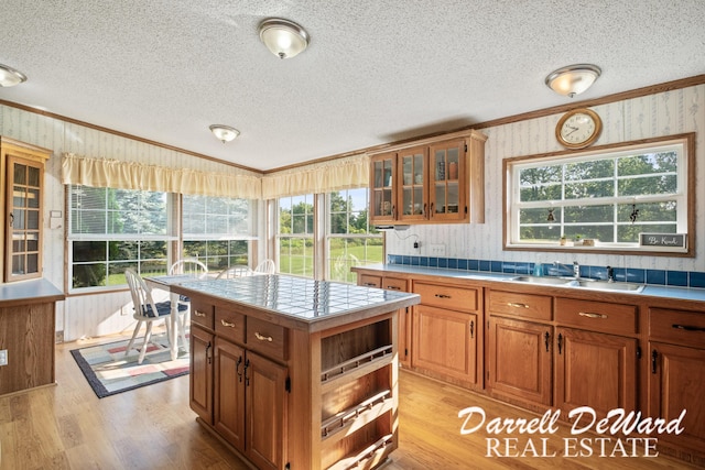 kitchen with sink, crown molding, light hardwood / wood-style flooring, tile counters, and a kitchen island