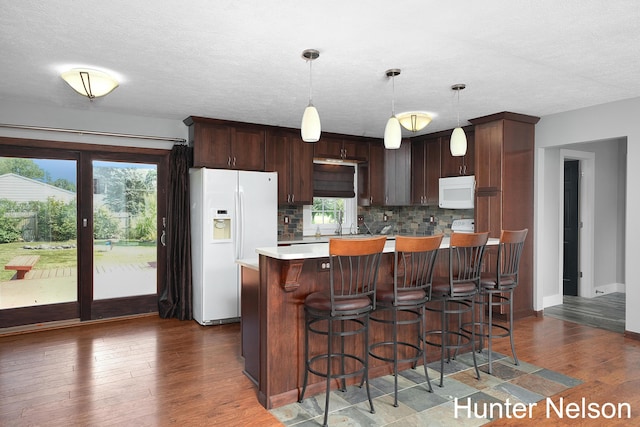 kitchen with backsplash, hanging light fixtures, a center island, dark brown cabinetry, and white appliances