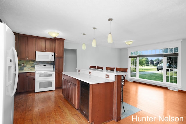 kitchen with tasteful backsplash, a kitchen bar, hanging light fixtures, a center island, and white appliances