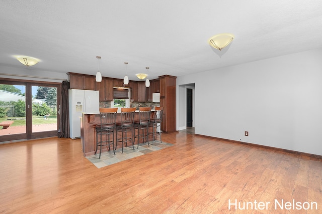 kitchen featuring pendant lighting, backsplash, a kitchen bar, a center island, and white appliances