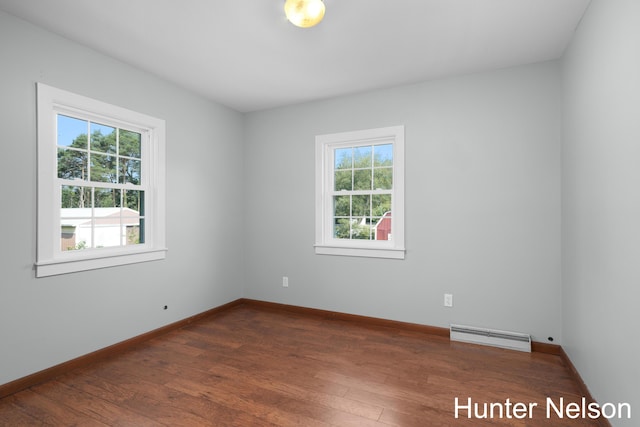 empty room featuring a baseboard radiator, plenty of natural light, and dark wood-type flooring