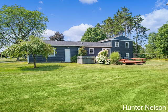 back of property featuring a wooden deck, a yard, and a hot tub