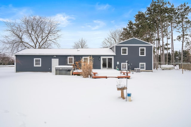 snow covered rear of property with a hot tub, central AC unit, and a wooden deck