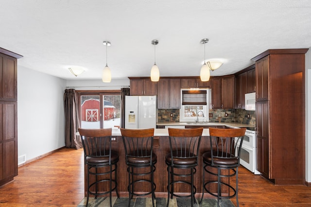 kitchen with hanging light fixtures, a center island, sink, white appliances, and decorative backsplash