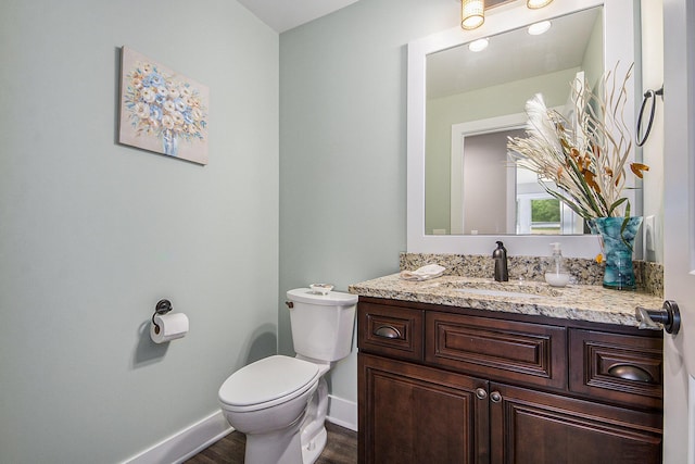 bathroom with vanity, toilet, wood finished floors, and baseboards