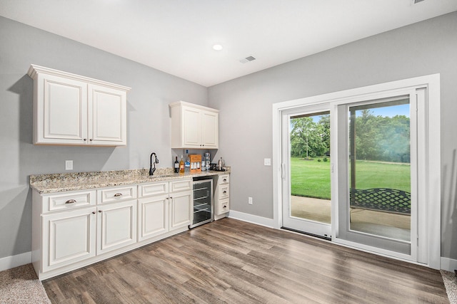 bar featuring wood-type flooring, wine cooler, and light stone countertops