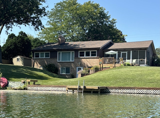 back of house with a water view, a sunroom, a storage unit, and a lawn