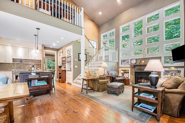 living room featuring a towering ceiling, sink, wooden ceiling, and light wood-type flooring