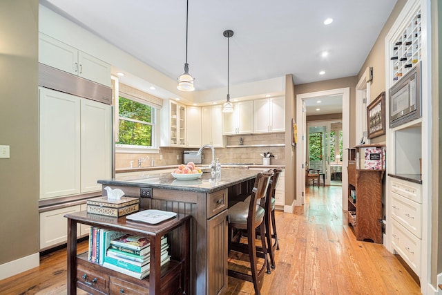 kitchen featuring white cabinetry, a kitchen island with sink, and dark stone countertops