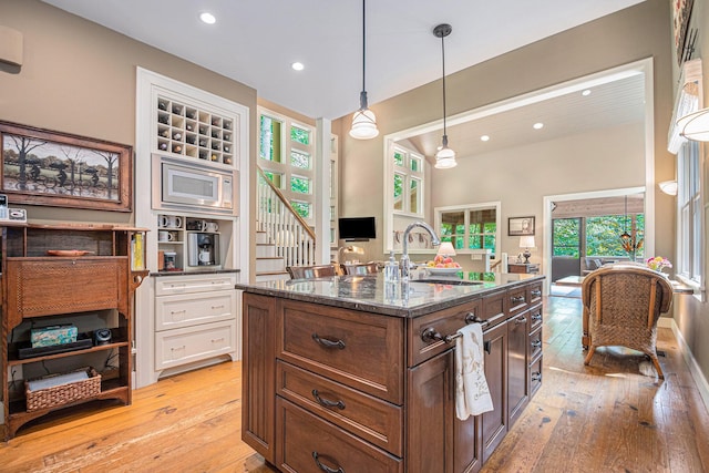 kitchen featuring pendant lighting, sink, white cabinetry, stainless steel microwave, and light hardwood / wood-style floors