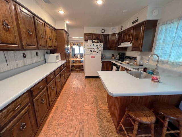 kitchen with sink, a breakfast bar area, white appliances, kitchen peninsula, and light wood-type flooring