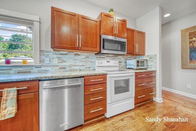 kitchen featuring backsplash, light hardwood / wood-style flooring, light stone countertops, and appliances with stainless steel finishes