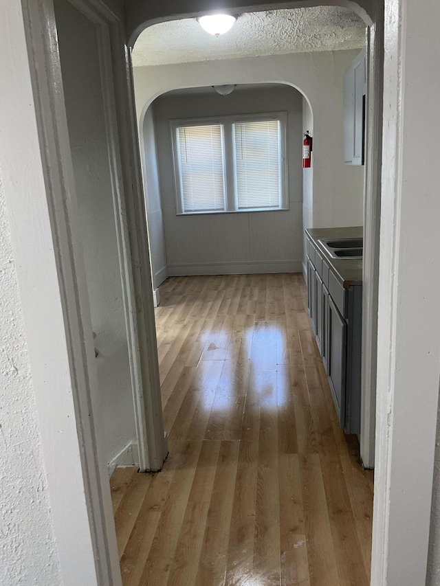 corridor with sink, light hardwood / wood-style floors, and a textured ceiling