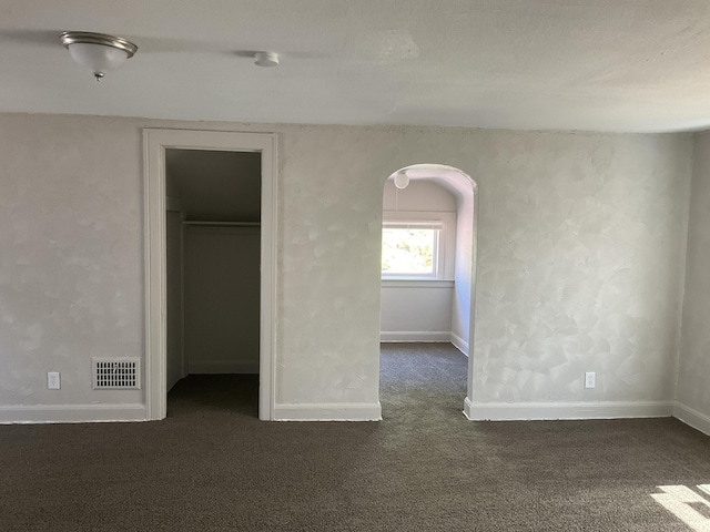 unfurnished bedroom with dark carpet, a walk in closet, and a closet