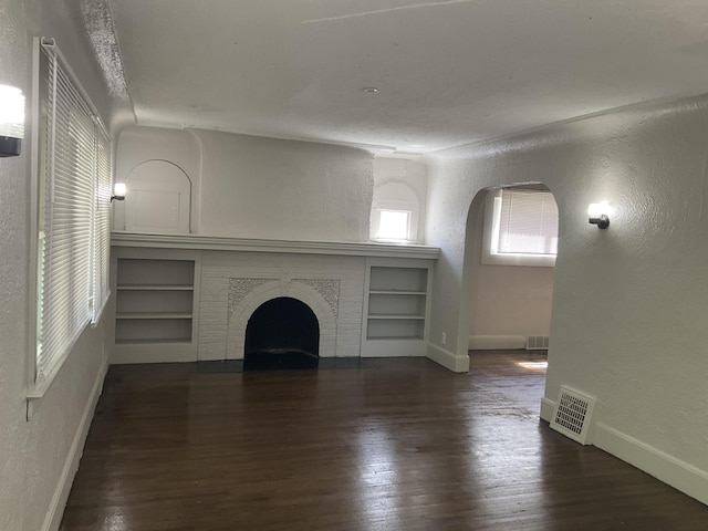 unfurnished living room featuring dark hardwood / wood-style flooring, a fireplace, built in features, and a healthy amount of sunlight