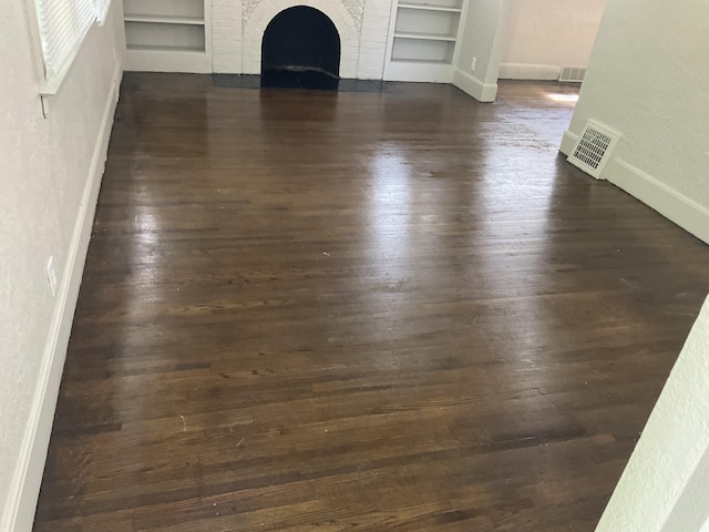 unfurnished living room with dark wood-type flooring, a fireplace, and built in shelves