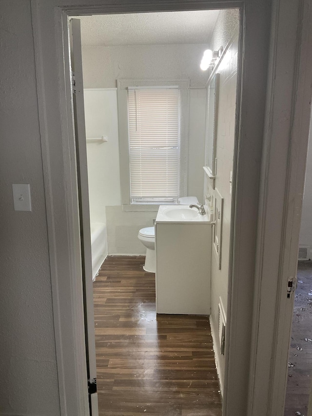 bathroom featuring vanity, a tub to relax in, hardwood / wood-style floors, and toilet