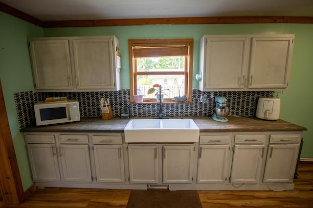 kitchen with tasteful backsplash, white cabinetry, sink, and light wood-type flooring