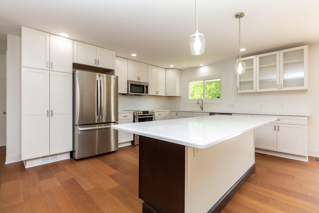 kitchen with stainless steel appliances, decorative light fixtures, wood-type flooring, a kitchen island, and white cabinets