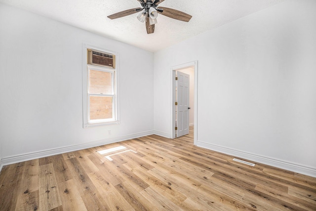 empty room with ceiling fan, light hardwood / wood-style flooring, a wall mounted AC, and a textured ceiling