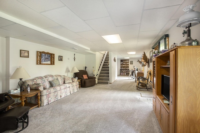 carpeted living room with a drop ceiling and stairs