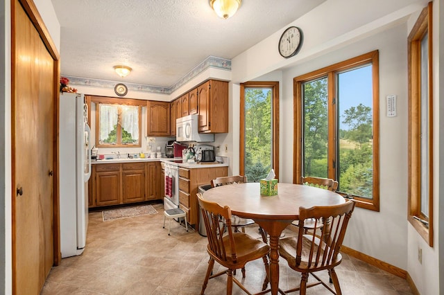 kitchen with baseboards, light countertops, brown cabinets, white appliances, and a textured ceiling