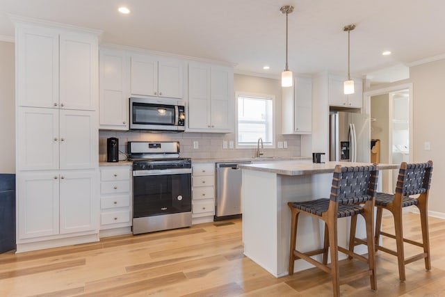 kitchen with appliances with stainless steel finishes, white cabinetry, ornamental molding, a kitchen island, and decorative light fixtures