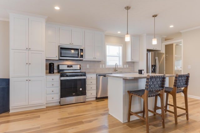 kitchen with pendant lighting, ornamental molding, stainless steel appliances, and white cabinets