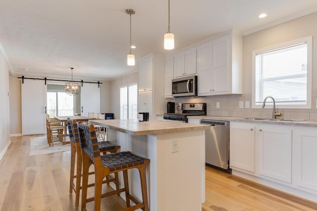 kitchen featuring pendant lighting, sink, white cabinetry, stainless steel appliances, and a center island